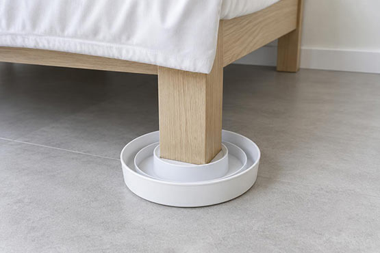 Bed bug interceptor positioned beneath a wooden bed leg